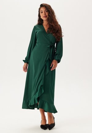Groene wikkeljurk van gladde stof, met lange mouwen, een strikceintuur en een gerimpelde zoom. Elegante jurk tot op de grond.