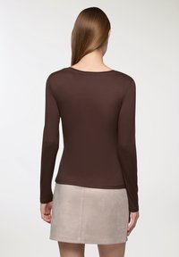 Brązowa koszula z długim rękawem o gładkiej fakturze, okrągłym dekolcie i dopasowanym kroju, zestawiona z jasnobeżową spódnicą z zamszu.