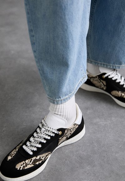 Sorte og beige slangeprint sneakers med hvide såler og snørebånd, parret med lyseblå denim bukser og hvide sokker.