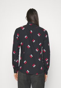 Czarna koszula z czerwono-białym nadrukiem "HUGO", długie rękawy, klasyczny kołnierzyk oraz mankiety na guziki. Gładki materiał, luźny krój.