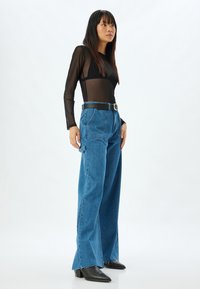 Top negro transparente de manga larga con un diseño triangular, combinado con jeans de mezclilla azul de pierna recta de tiro alto y un cinturón negro.
