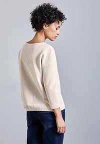 Helle beige, gerippte Strickjacke mit lässigem Schnitt, ¾-Ärmeln und rundem Ausschnitt, kombiniert mit dunkelblauen Jeans.