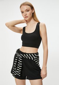 Sort figursyet crop top med brede stropper, parret med løse sorte shorts, der har et kontrasterende sort-hvidt stribet bånd omkring taljen.