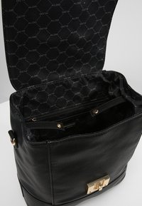 Czarna torebka o teksturowanej powierzchni z złotym zapięciem, wyposażona w kieszeń na suwak oraz wnętrze wyściełane materiałem z firmowym wzorem. Otwarty wierzch.