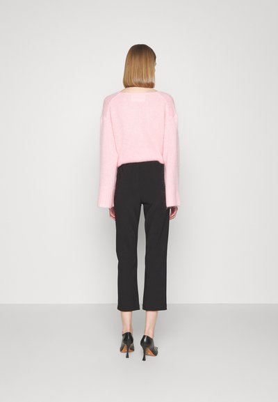 Pink, oversized sweater with dropped shoulders and ribbed cuffs paired with black, cropped trousers and black pointed heels. Simple design.