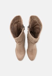 Paire de bottines mi-mollet en suède marron clair avec des fermetures éclair côté intérieur et des tiges supérieures légèrement affaissées, vues de dessus sur fond blanc.