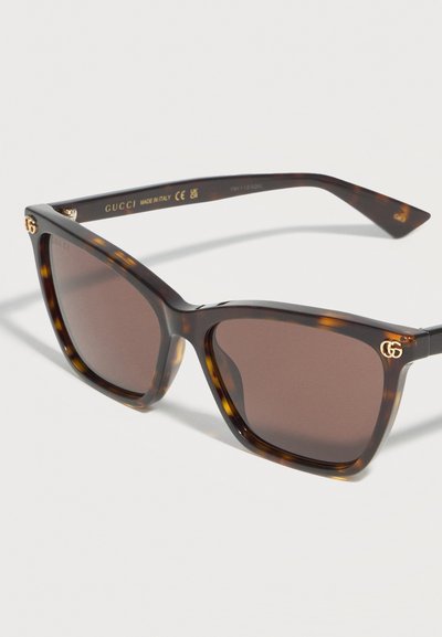 Ηλιακά γυαλιά Gucci με καφέ φακούς σε τετράγωνο σχήμα και χρυστό λογότυπο GG στις πάνω γωνίες της θήκης, με σχέδιο χελώνας.