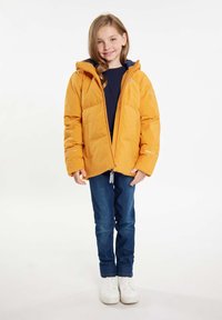 Gul puffjacka med huva, med en framzip och elastiska ärmslut. Bärs över en mörk topp, ihop med blå jeans och vita sneakers.