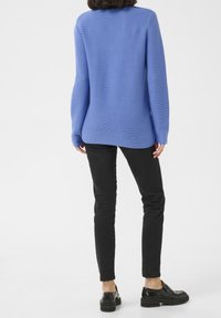 Suéter azul de punto acanalado con manga larga, dobladillo trasero ligeramente más largo que el delantero, combinado con pantalones negros ajustados y zapatos negros.