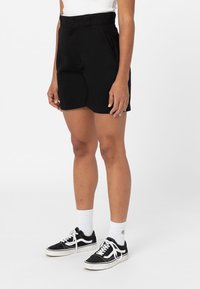 Černé bermudové šortky vyrobené z lehkého materiálu, s vysokým pasem a bočními kapsami, doplněné černými teniskami a bílými ponožkami.