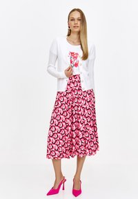 Biały sweter dziany noszony na białej bluzce z kwiatowym wzorem, połączony z różową spódnicą plisowaną z serduszkami. Jasnoróżowe obcasy dopełniają outfit.