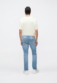 Helebeežide ribidega lühikeste varrukatega särk, kombineeritud hele siniste kitsaste teksadega. Valged tossud täiendavad komplekti. Silt on teksadel nähtaval.