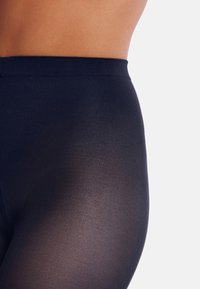 Leggings blu navy con una texture liscia e semi-trasparente. La vita è elastica, offrendo una vestibilità aderente. Nessun motivo o accessorio visibile.