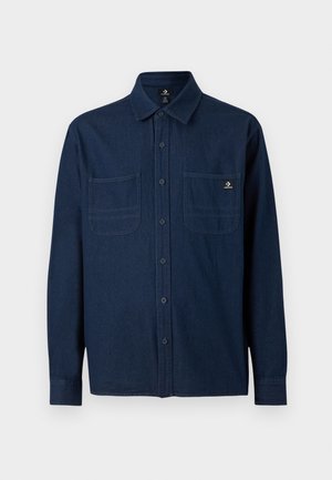 Laivastonsininen pitkähihainen nappipaita, jossa on kaksi rintataskua ja pieni Converse-logo oikeassa taskussa.