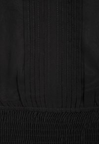 Svart tyg med vertikala veck upptill som övergår i samlad, elastisk textur nertill. Mjukt, lätt material.