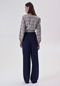 B blouse corto a quadre grigio chiaro con maniche lunghe abbinato a pantaloni navy a gamba larga. Tessuto liscio e vestibilità rilassata.