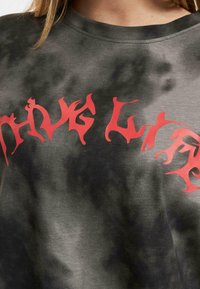 Grafický tričko s černobílým tie-dye vzorem a výrazným červeným textem "Žij život" v abstraktním písmu.