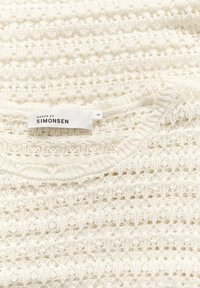 Stickad tröja i off-white, med ett öppet virkmönster, rundad halsringning och etikett med texten "KAREN BY SIMONSEN" i svart. Storlek M.
