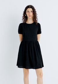 Schwarzes Kurzarmkleid aus strukturiertem Stoff, mit Rundhalsausschnitt und gerafftem Rock, das einen taillierten Oberteil und einen ausgestellten Saum hat.