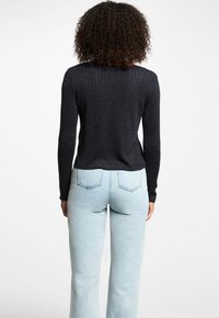 Zwarte geribde trui met lange mouwen, gemaakt van een gestructureerd materiaal, heeft een subtiele metallic glans. Combinatie met lichtblauwe hoog-getailleerde jeans.