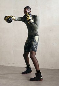 Mann in schwarzen und goldenen Boxhandschuhen und Shorts, der in einem kahlen Innenraum einen geraden Schlag ausführt.