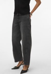 Jeans neri a vita alta con taglio morbido, leggera scoloritura e cuciture tonali; abbinati a tacchi slingback neri con punta affusolata.