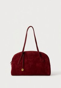 Červená semišová kabelka s kulatým tvarem, dvěma dlouhými uchy a zlatým kováním. Hladká textura s jemným leskem.