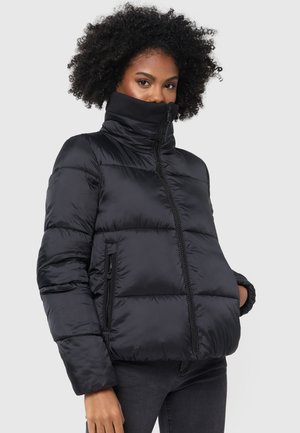 Black puffer jacket with high collar, quilted design, zippered pockets, and soft texture. Worn over dark jeans, showcasing a modern cut.