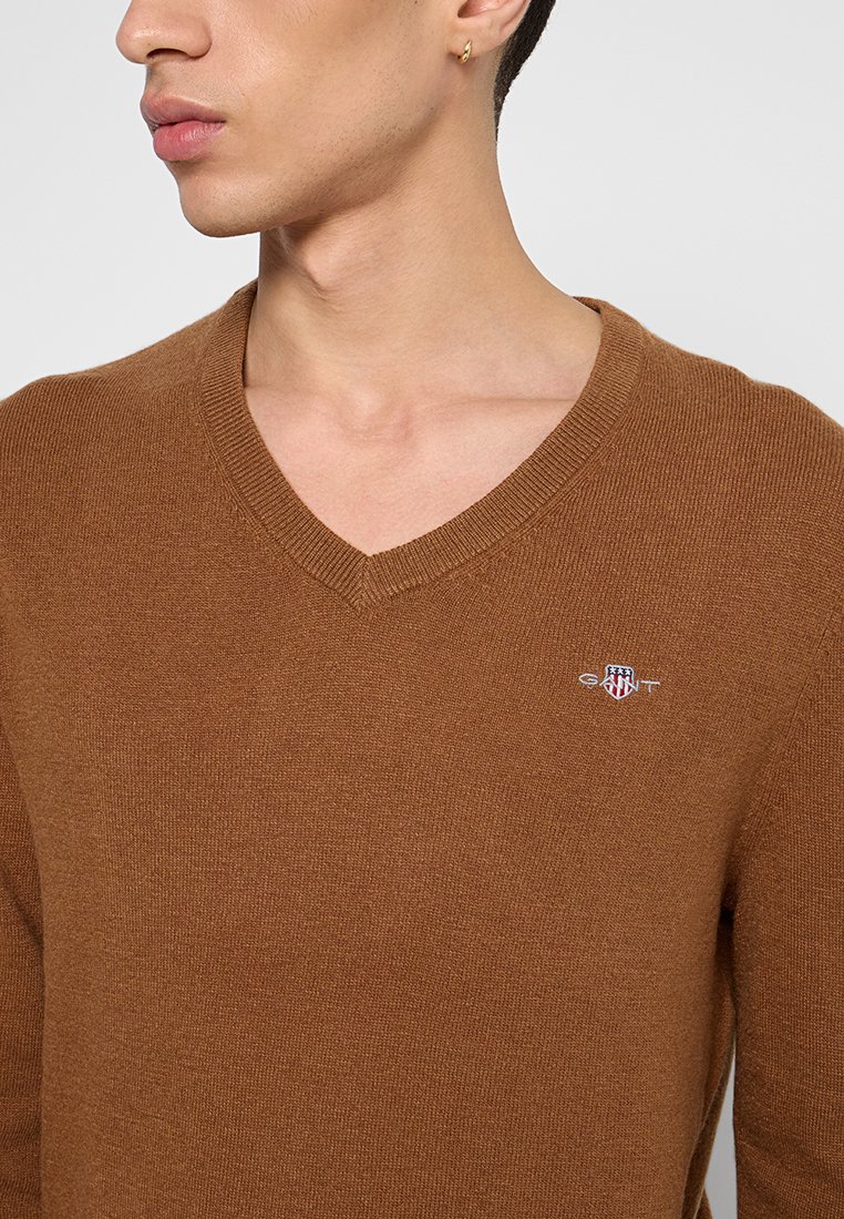 Brauner Baumwoll-V-Ausschnitt-Pullover mit gerippter Textur und kleinem gesticktem Logo auf der linken Brust. Die Passform ist lässig mit einer schlanken Silhouette.