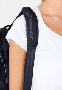 Schwarzer Babolat-Rucksack mit gepolstertem Schultergurt, der mit einem Logo und gestreiften Akzenten versehen ist. Der Gurt hat eine strukturierte Oberfläche und ist für Komfort ausgelegt.