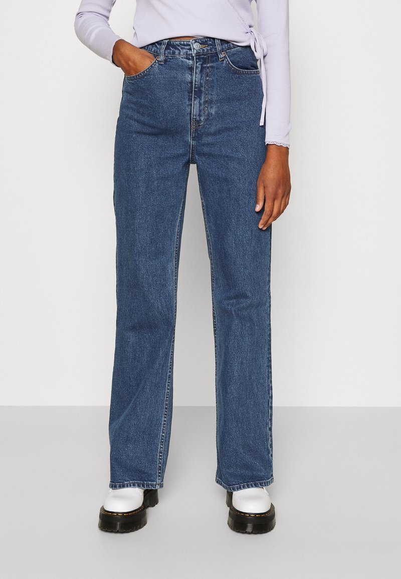 Blå denimjeans med hög midja, rak benpassform, femficksdesign och kontrasterande sömmar, kombinerat med svarta platåskor.