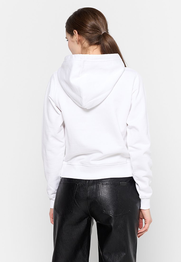 Hoodie en coton blanc avec une capuche à cordon de serrage, des poignets et un ourlet côtes. Associé à un pantalon en simili cuir noir.