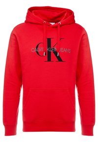 Punainen huppari, joka on valmistettu pehmeästä kankaasta. Hupparissa on etutasku ja rohkea musta "CK"-logo, jonka alla lukee "CALVIN KLEIN JEANS".
