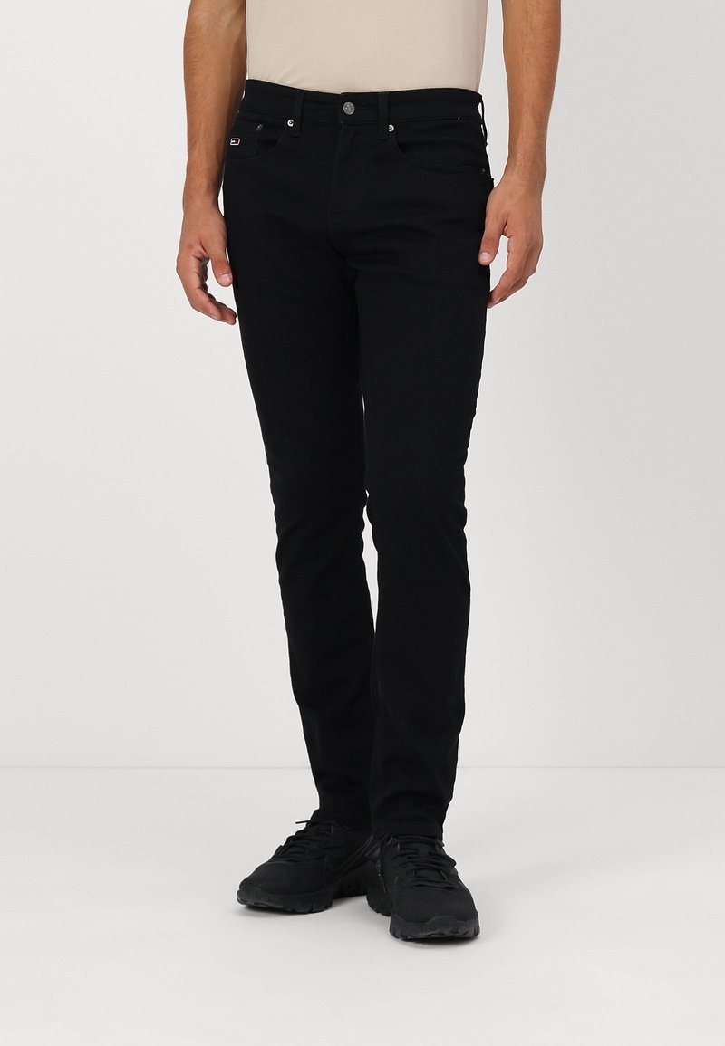 Zwarte spijkerbroeken van denim, met een slim fit ontwerp, vijf zakken en metalen hardware, gecombineerd met zwarte sportschoenen.