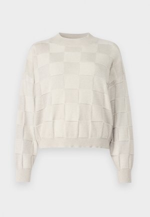 Vaaleanbeige, lyhyt neulepusero, jossa on teksturoitu ruutukuosi, pyöreä pääntie ja ribbaustaskut. Pehmeä materiaali, jossa on hienovarainen kiilto.
