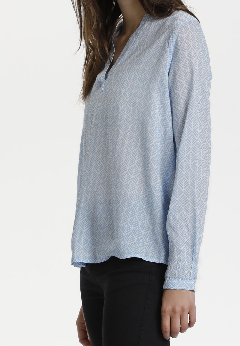 Långärmad ljusblå blus med ett mönstrat lövdesign, som har en liten krage och en avslappnad passform, gjord av ett slätt tyg.