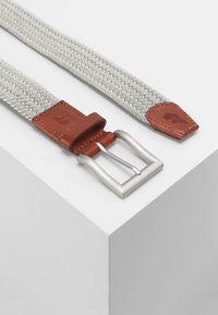 Cintura intrecciata grigia chiara con accenti in pelle marrone e una fibbia in metallo argentato lucido, caratterizzata da una superficie testurizzata e estremità affusolate.