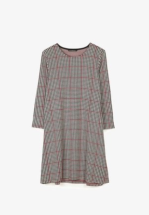 Sukienka z długim rękawem w czarno-biały wzór pepitki, pokryta cienkimi czerwonymi liniami tworzącymi kratę, z okrągłym dekoltem.