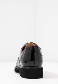 Scarpe in pelle verniciata nera con design brogue, caratterizzate da rifiniture dettagliate e una suola nera testurizzata. Finitura liscia, tacco basso.