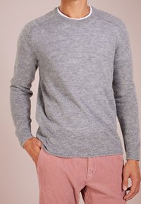 Grauer Wollpullover mit rundem Ausschnitt und langen Ärmeln. Hat eine glatte Textur und gerippte Bündchen, getragen mit hellrosa Cordhosen.