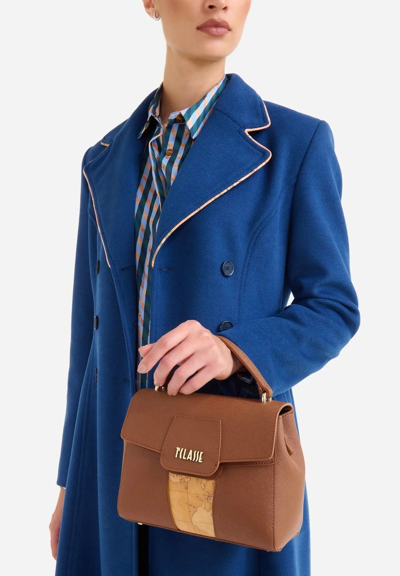 Borsa a tracolla in similpelle marrone con design a mappa sulla parte anteriore, ferrature dorate e forma strutturata. Indossata con un cappotto blu e una camicia a fantasia.