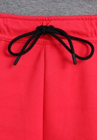 Röda sweatpants med elastisk midja och svart dragsko. Tyget ser slätt och stretchigt ut, med två framfickor.