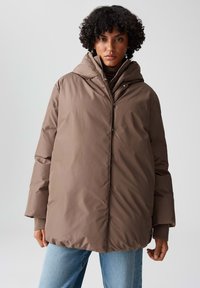 Giacca imbottita marrone con cappuccio, dotata di cerniera frontale e chiusura a scatto. Il materiale ha una texture liscia, con maniche larghe e orlo arrotondato.