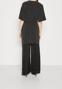 Top nero scintillante a maniche corte con vita elastica, abbinato a pantaloni neri a gamba larga e liscia. Texture morbide in tutto.