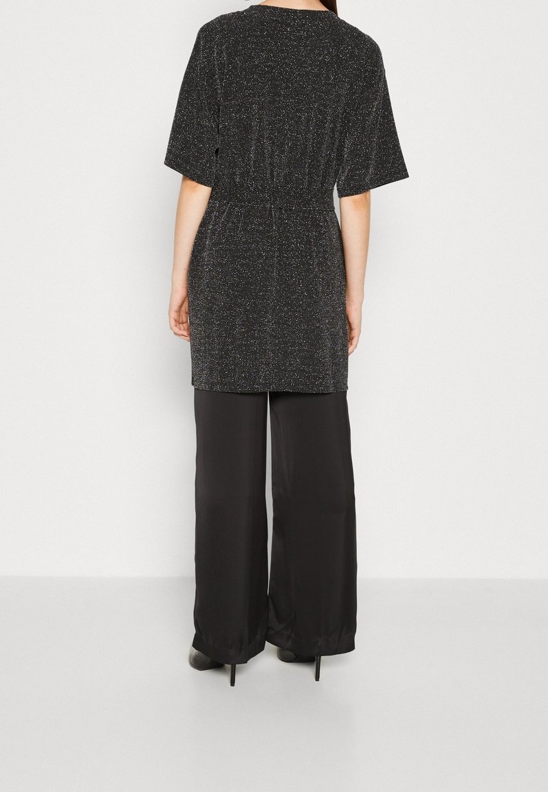 Top nero scintillante a maniche corte con vita elastica, abbinato a pantaloni neri a gamba larga e liscia. Texture morbide in tutto.