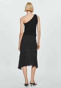 Top nero con una spalla abbinato a una gonna midi nera con pois. Tessuto liscio, design fluido e vita aderente. Sandali neri con tacco.