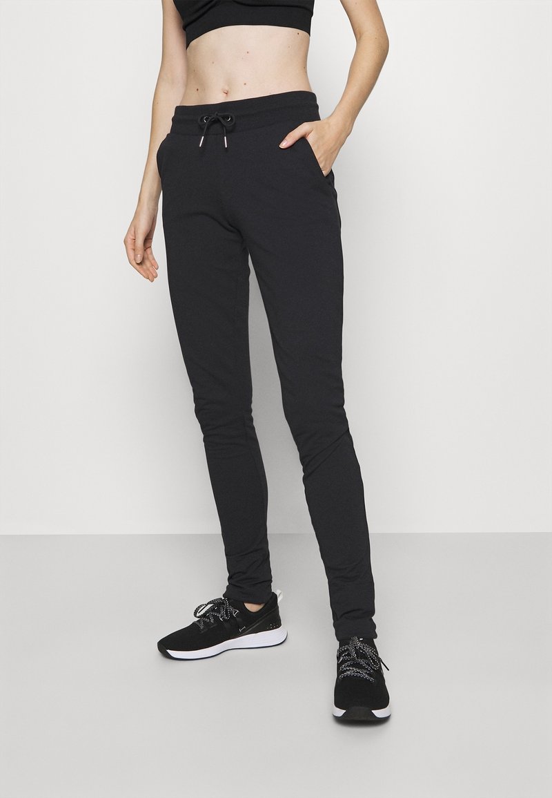 Zwarte joggerbroek met een tailleband met trekkoord, zijzakken en taps toelopende pijpen, gedragen met zwarte sneakers en een bijpassend cropped topje.