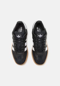 Black leather sneakers with suede accents, three white stripes, and a gum rubber sole. Features padded tongue and black laces.