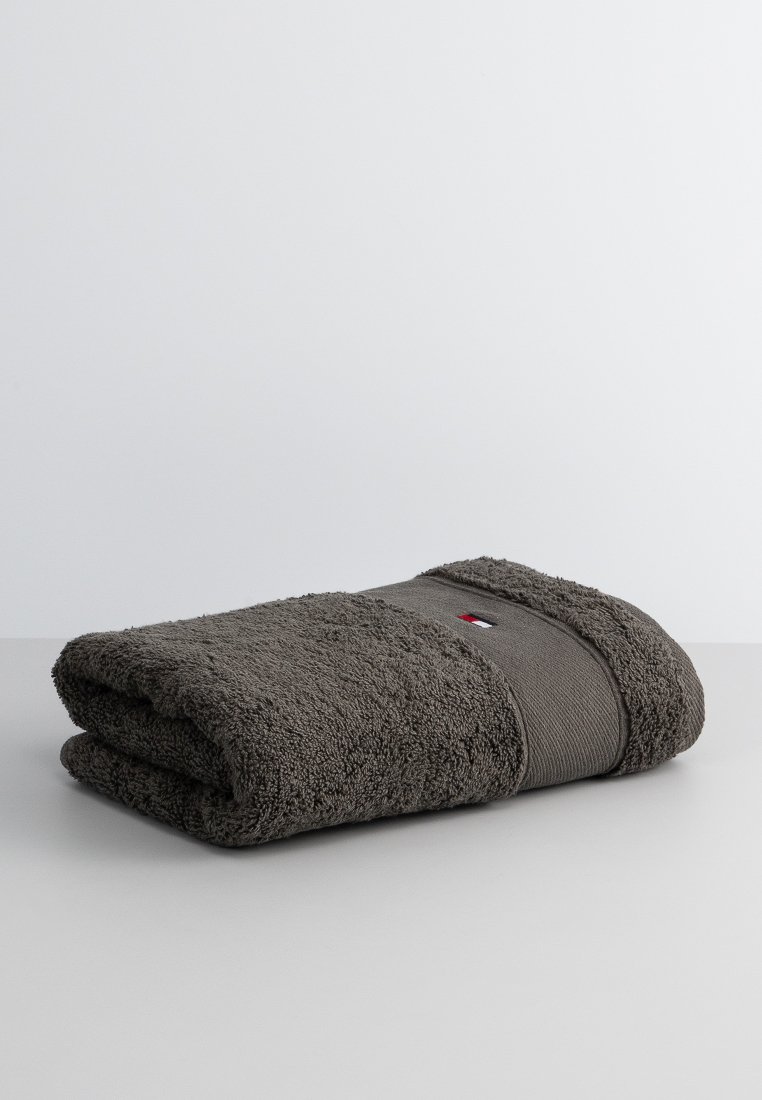 Donkergrijze handdoek, van een gestructureerd terrycloth materiaal met een gladde grijze band over het midden. Voorzien van een klein logo-label in rood, wit en blauw.