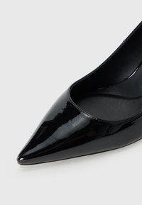 Sorte patentlærstøvle med spiss tå og en glatt overflate, med lavskåret design og strukturert innersåle.